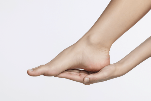 mão sustentando pé com foco na fáscia plantar, indicando dor típica de fascite plantar. Pronto para fazer um exercício para fascite plantar. levanta a pergunta, fascite o que é?